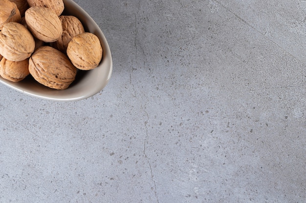 Cuenco gris de nueces sin cáscara orgánicas sobre fondo de piedra.