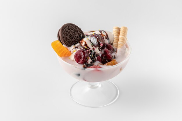 Cuenco de helado con yogur helado fresco, frutas, galletas y cerezas aislado sobre un fondo blanco y gris con sombras naturales