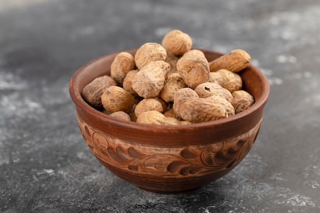 Cuenco lleno de cacahuetes con cáscara saludables colocados sobre una mesa de piedra.