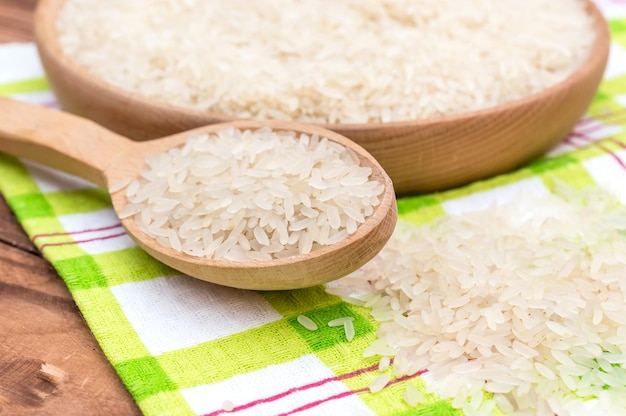 Cuenco de madera de arroz crudo y cuchara de madera en una mesa de madera