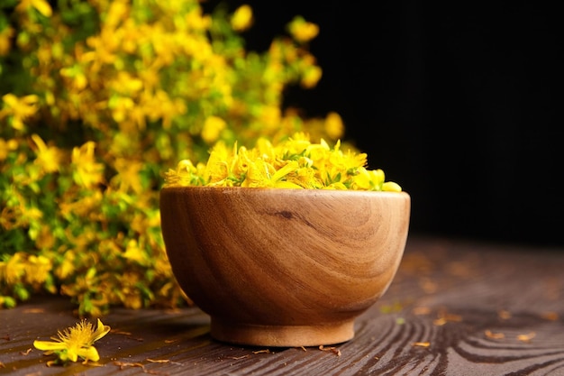 Cuenco de madera con Hypericum perforatum o hierba de San Juan capullos sobre fondo oscuro