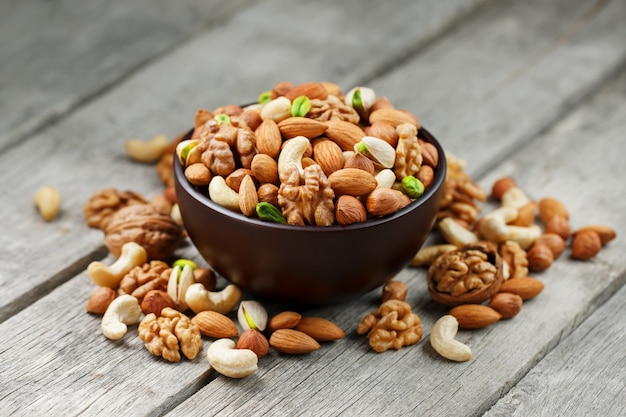 Cuenco de madera con nueces mixtas en un gris de madera. Nueces, pistachos, almendras, avellanas y anacardos, nueces.