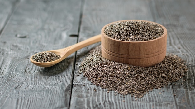 Cuenco de madera con semillas de Chia negro y cuchara de madera sobre la mesa rústica.