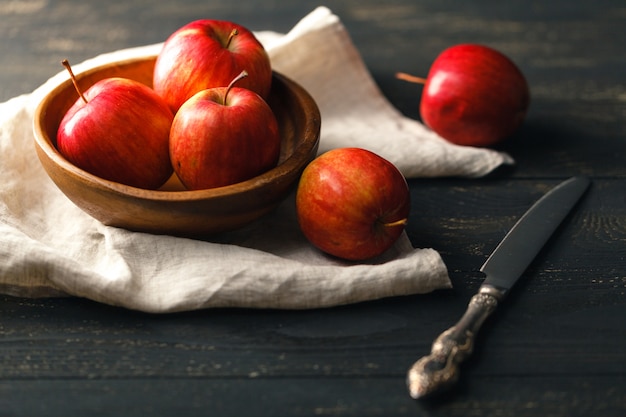 Un cuenco con manzanas rojas de otoño sobre una superficie de madera oscura con textiles. Horizontal