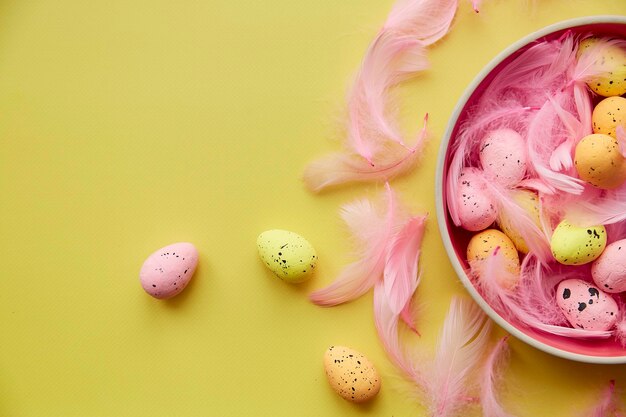 Cuenco de Pascua minimalista sobre toalla con huevos de colores y plumas rosas sobre fondo amarillo Copiar espacio