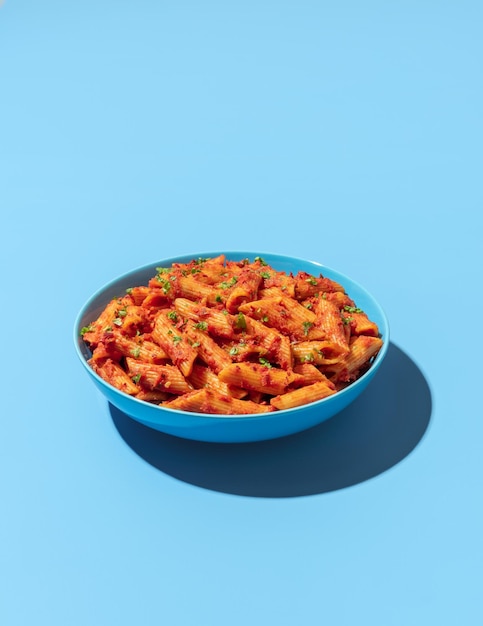 Cuenco de pasta Penne aislado sobre un fondo azul.