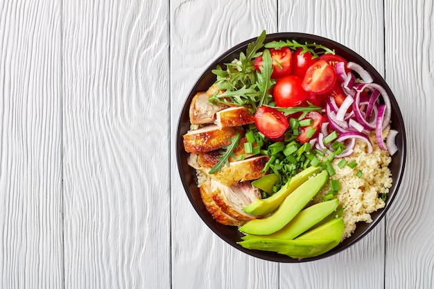 cuenco de pollo con cuscús, verduras, aguacate, cebollín y rúcula