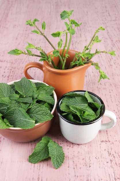 Cuenco redondo marrón y taza de metal blanco de hojas de menta fresca y taza de ramas de menta sobre fondo de madera rosa