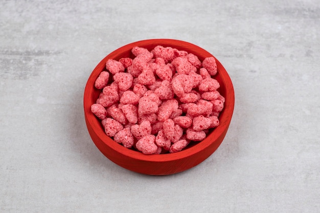 Cuenco rojo lleno de cereales rosados en piedra.