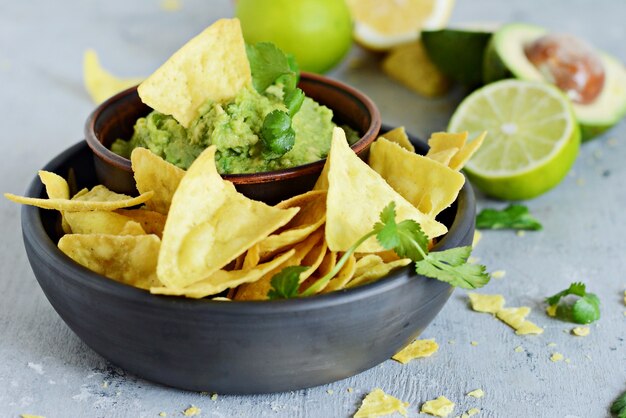 Cuenco de salsa de guacamole con nachos de maíz (chips) e ingredientes sobre un fondo azul, enfoque selectivo. Plato nacional mexicano.