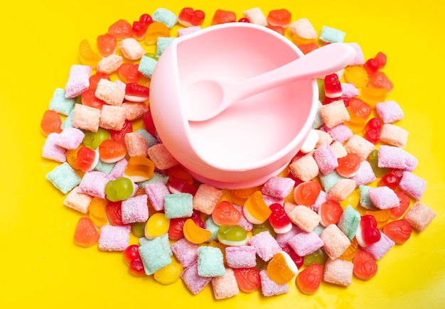 Cuenco de silicona para vajilla infantil con cuchara. Sirviendo comida para bebés, vajilla para niños. El cuenco y la cuchara de silicona rosa están en un montón de dulces y mermelada. foto brillante y colorida.