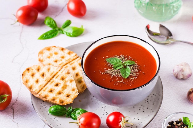 Cuenco con sopa de tomate casera con albahaca y verduras frescas sobre la mesa