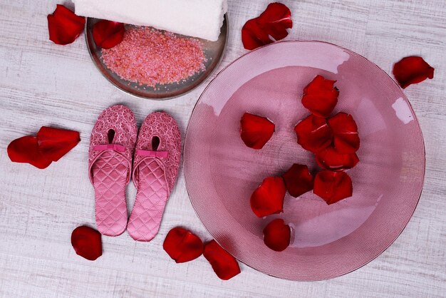 Cuenco de spa con agua, pétalos de rosa, toalla y zapatillas sobre fondo claro. Concepto de pedicura o tratamiento de spa natural