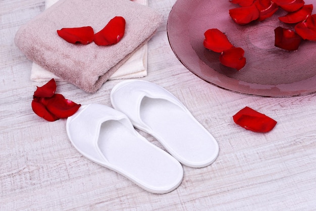 Cuenco de spa con agua, pétalos de rosa, toalla y zapatillas sobre fondo claro. Concepto de pedicura o tratamiento de spa natural