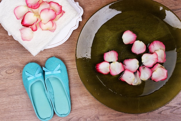 Cuenco de spa con toalla de pétalos de rosa de agua y zapatillas sobre fondo claro Concepto de pedicura o tratamiento de spa natural