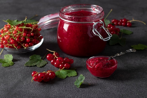 Cuenco y tarro de cristal de mermelada de grosella roja casera sobre un fondo oscuro Primer plano