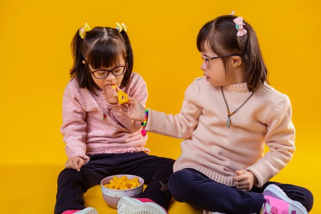 Cuencos con bocadillos. Agradable chica morena proponiendo papas fritas a su hermana siendo agradable y amable