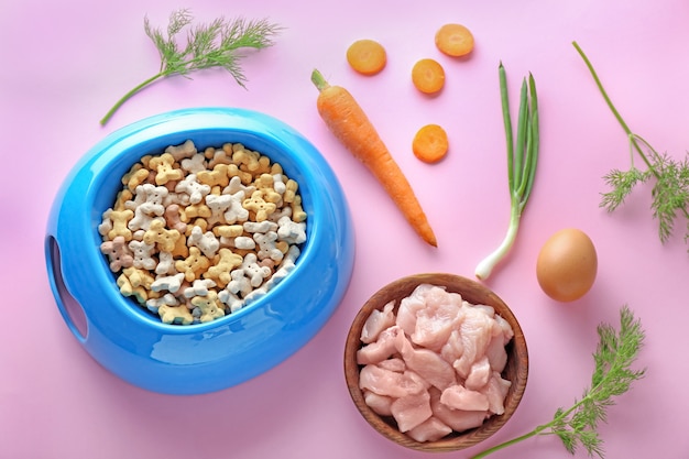 Cuencos con comida para mascotas y productos naturales sobre fondo de color