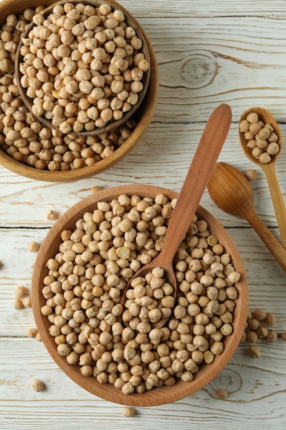 Cuencos y cucharas con garbanzos sobre mesa de madera blanca