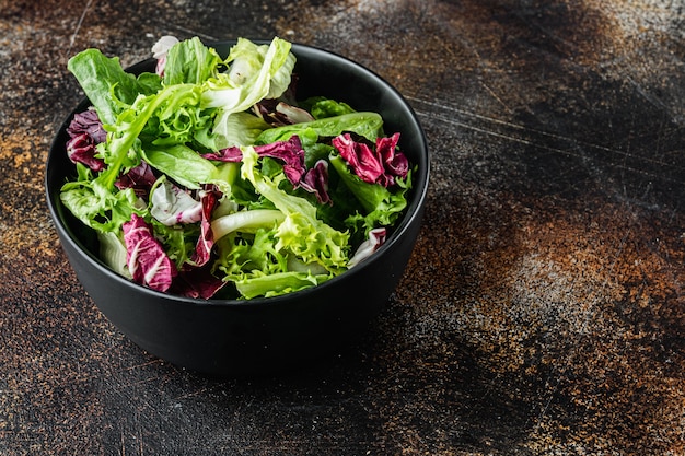 Cuencos con ensalada de lechuga rallada mixta hojas frescas, sobre fondo rústico oscuro antiguo con espacio para copiar texto