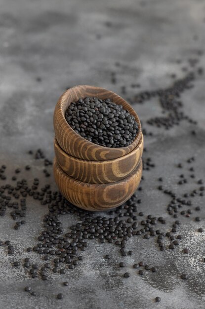 Cuencos de madera de lentejas negras secas sobre una mesa gris cerca de la fuente de proteínas para la dieta vegetariana