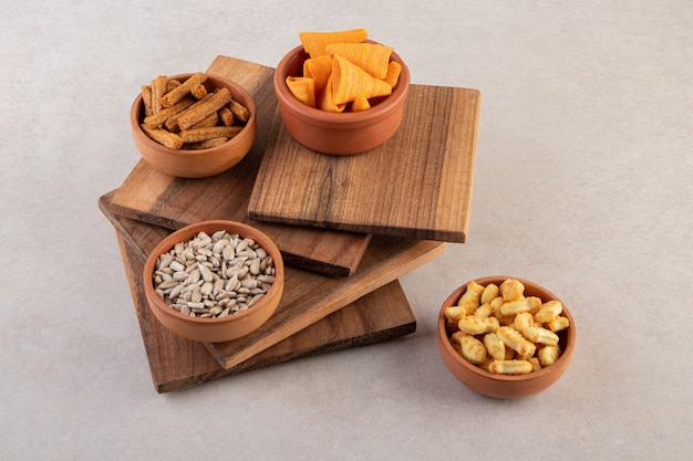 Cuencos de patatas fritas, galletas saladas y semillas de girasol en la superficie de la piedra.