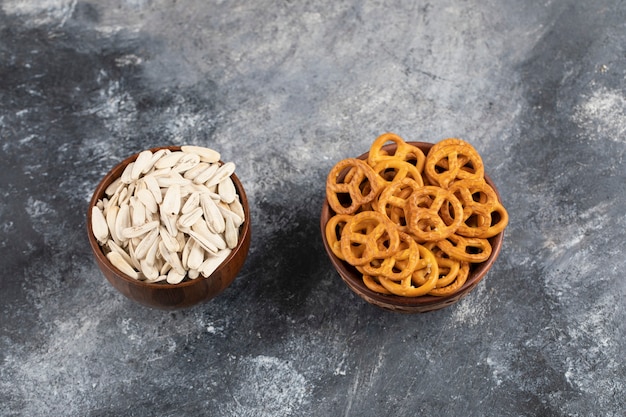 Cuencos de pretzels secos salados y semillas de girasol blancas sobre superficie de mármol