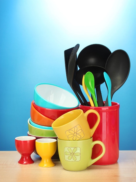 cuencos vacíos brillantes tazas y utensilios de cocina en una mesa de madera con fondo azul