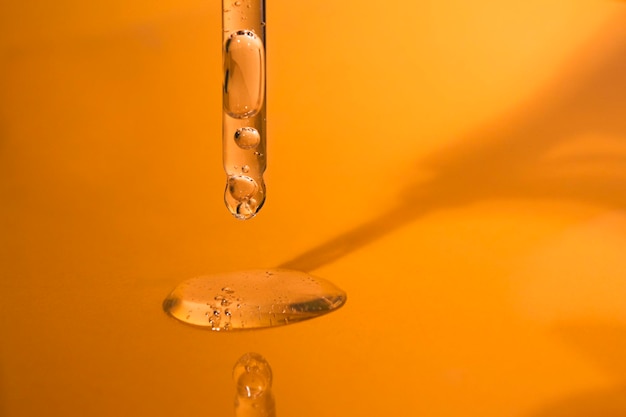 Cuentagotas de vidrio de primer plano con una textura cosmética líquida transparente sobre un fondo naranja brillante