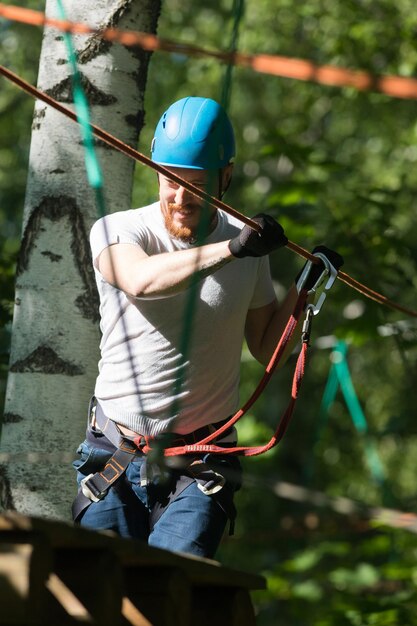 Cuerda aventura hombre sonriente caminando sobre el puente de cuerda atado al árbol con un gancho de seguro