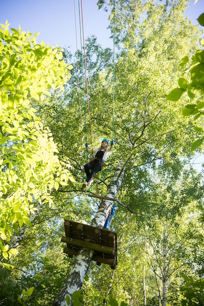 Cuerda aventura mujer rubia caminando de un puesto a otro cruzando la cuerda en el bosque