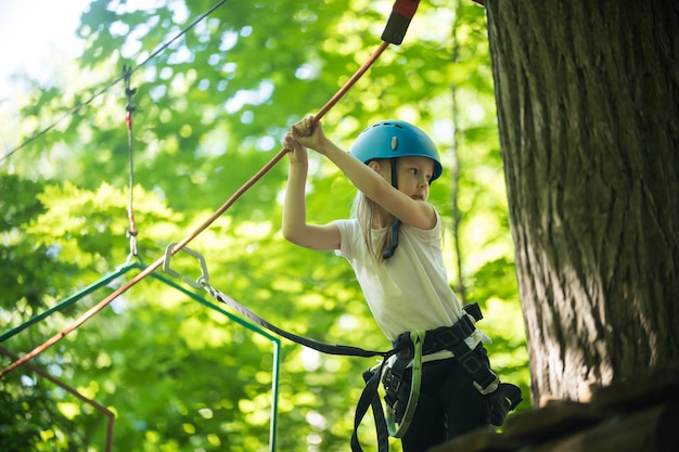 Cuerda aventura una niña de pie en lo alto por el árbol y sujetando las cuerdas con las manos