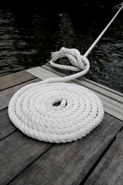 Una cuerda blanca de barco unida a un muelle de madera con agua oscura debajo