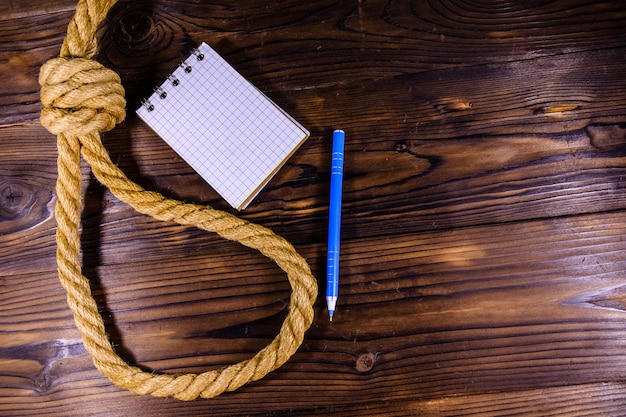 Cuerda con soga para el suicidio, bloc de notas en blanco y bolígrafo sobre fondo de madera
