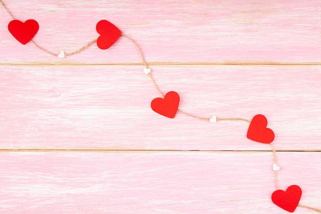 Cuerda de yute con corazones de brillo rojo y corazones de confeti sobre fondo rosa