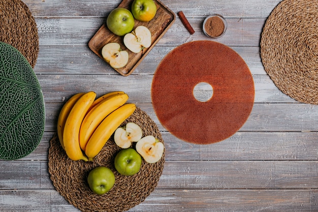 Cuero de fruta canela con frutas frescas en la mesa de madera. Cuero frutal redondo. Comida sana. Vista superior de manzanas, plátanos y canela.