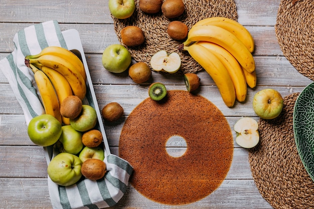 Cuero de fruta con frutas frescas en la mesa de madera. Cuero frutal redondo. Comida sana. Vista superior de manzanas, plátanos y kiwis.