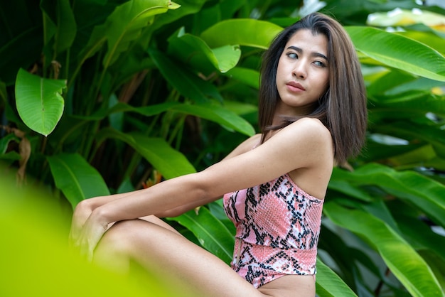 Cuerpo bronceado delgado de mujer joven en bikini en hojas de palma mujer pelirroja positiva con piel limpia y belleza natural de pie detrás de hojas tropicales concepto de cuidado de la piel de vacaciones de verano bikini en la naturaleza