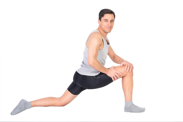 Foto cuerpo completo de deportista de contenido mirando a la cámara mientras estira el músculo psoas durante el entrenamiento de fitness aislado en fondo blanco en el estudio
