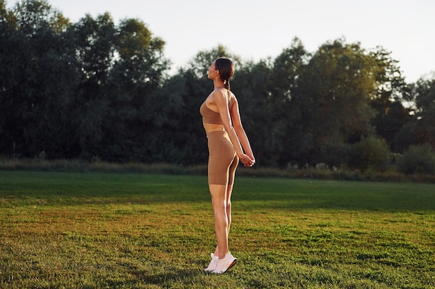 Cuerpo flexible Mujer joven en ropa de yoga está al aire libre en el campo