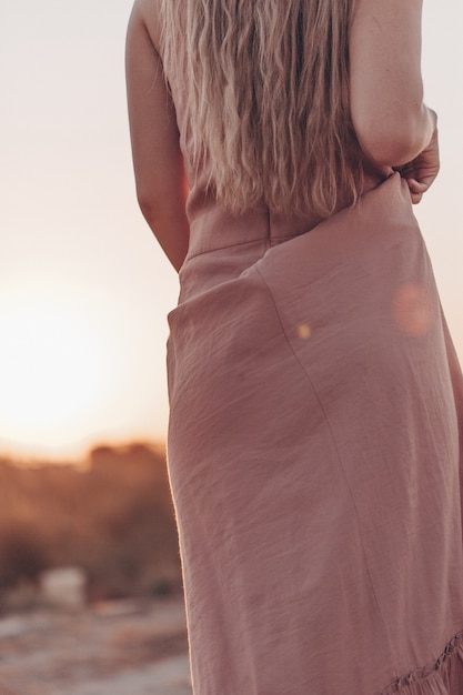 Cuerpo de joven hermosa mujer rubia caucásica en vestido rosa en un campo desierto en puesta de sol