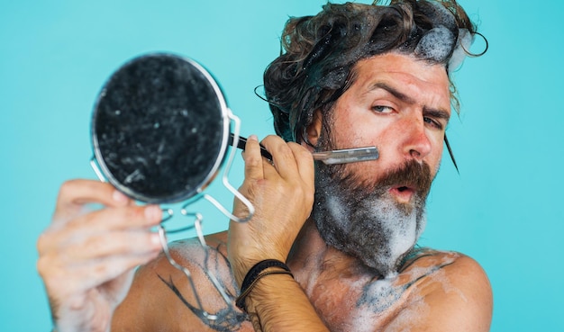 Cuidado de la barba afeitado masculino barbudo con navaja de afeitar mirando al espejo hombre tomando ducha spa