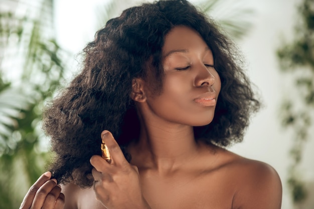 Cuidado del cabello. Atractiva mujer afroamericana rociando suero en su cabello