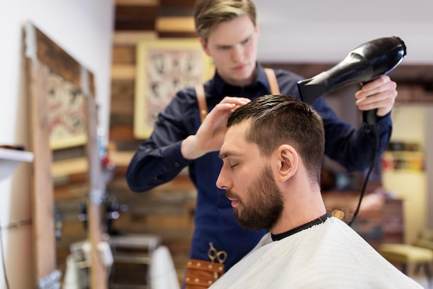 cuidado del cabello, peluquería y concepto de personas - hombre y peluquero o barbero con ventilador secando el cabello en la barbería