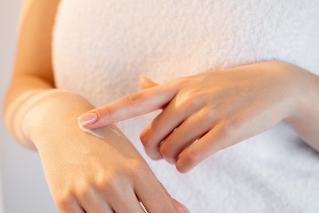 Cuidado del cuerpo Belleza de la piel de las manos Nutrición suave Mujer irreconocible que cubre con una toalla que aplica crema en el brazo con fondo claro