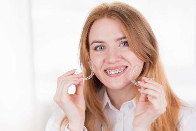 Cuidado dental Niña sonriente con frenos en los dientes sostiene alineadores en las manos y muestra la diferencia entre ellos