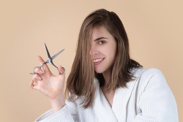 Cuidado do cabelo das mulheres. Retrato de mulher jovem feliz tendo o cabelo cortado com uma tesoura.