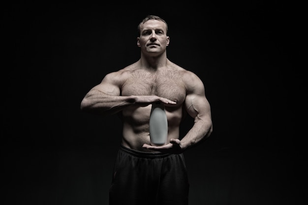 Cuidado e higiene corporal para deportistas. Bodybuilder mantenga la botella de champú o gel. Atleta hombre con torso en forma, six pack y ab. Cosmética de spa, baño o ducha después del entrenamiento en el gimnasio, vintage