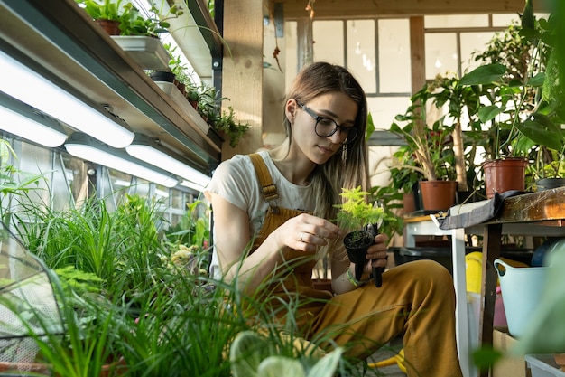 Cuidado de las hembras jóvenes de las plantas en macetas después del trabajo relajarse en el jardín interior floristería mujer emprendedora