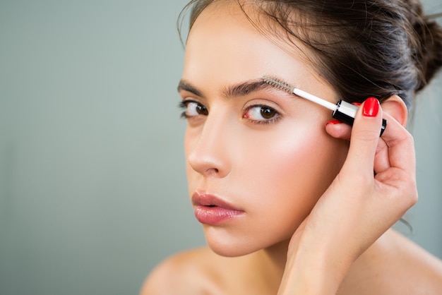 Cuidado maquillador de cejas aplicando un gel para cejas en las cejas de una mujer hermosa joven con defectos